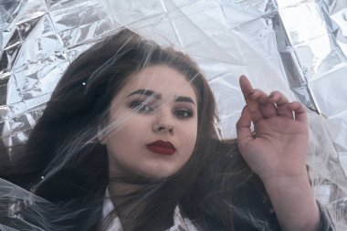 Tombul bir kızın güzel makyajı tül kumaşın altında altın bir folyonun üzerinde yatıyor..