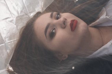 Tombul bir kızın güzel makyajı tül kumaşın altında altın bir folyonun üzerinde yatıyor..