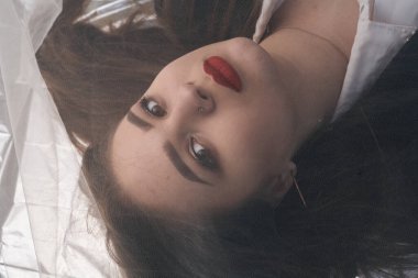 Tombul bir kızın güzel makyajı tül kumaşın altında altın bir folyonun üzerinde yatıyor..