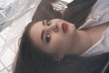 Tombul bir kızın güzel makyajı tül kumaşın altında altın bir folyonun üzerinde yatıyor..