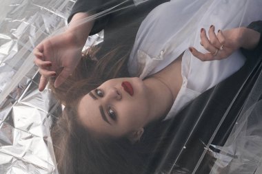 Tombul bir kızın güzel makyajı tül kumaşın altında altın bir folyonun üzerinde yatıyor..