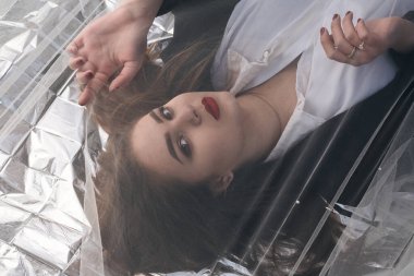 Tombul bir kızın güzel makyajı tül kumaşın altında altın bir folyonun üzerinde yatıyor..