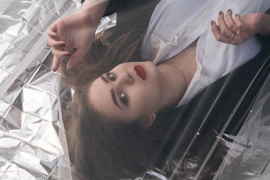 Tombul bir kızın güzel makyajı tül kumaşın altında altın bir folyonun üzerinde yatıyor..