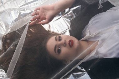 Tombul bir kızın güzel makyajı tül kumaşın altında altın bir folyonun üzerinde yatıyor..