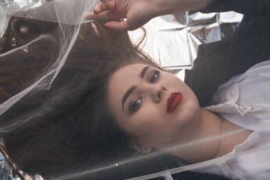 Tombul bir kızın güzel makyajı tül kumaşın altında altın bir folyonun üzerinde yatıyor..