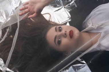 Tombul bir kızın güzel makyajı tül kumaşın altında altın bir folyonun üzerinde yatıyor..