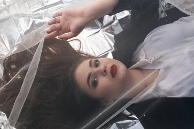 Tombul bir kızın güzel makyajı tül kumaşın altında altın bir folyonun üzerinde yatıyor..