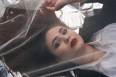 Tombul bir kızın güzel makyajı tül kumaşın altında altın bir folyonun üzerinde yatıyor..