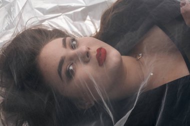 Tombul bir kızın güzel makyajı tül kumaşın altında altın bir folyonun üzerinde yatıyor..