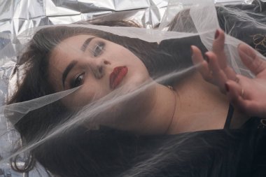 Tombul bir kızın güzel makyajı tül kumaşın altında altın bir folyonun üzerinde yatıyor..