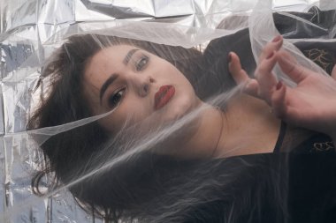 Tombul bir kızın güzel makyajı tül kumaşın altında altın bir folyonun üzerinde yatıyor..