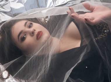 Tombul bir kızın güzel makyajı tül kumaşın altında altın bir folyonun üzerinde yatıyor..