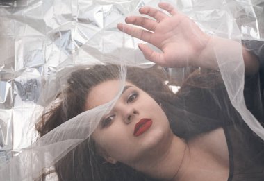 Tombul bir kızın güzel makyajı tül kumaşın altında altın bir folyonun üzerinde yatıyor..