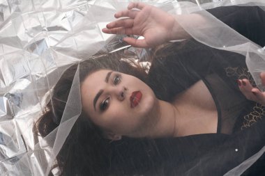 Tombul bir kızın güzel makyajı tül kumaşın altında altın bir folyonun üzerinde yatıyor..