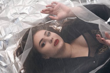 Tombul bir kızın güzel makyajı tül kumaşın altında altın bir folyonun üzerinde yatıyor..