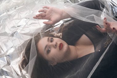 Tombul bir kızın güzel makyajı tül kumaşın altında altın bir folyonun üzerinde yatıyor..