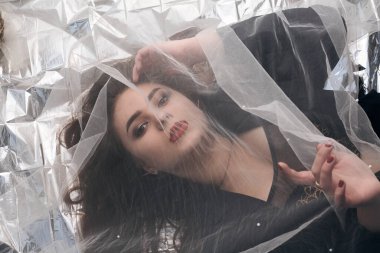 Tombul bir kızın güzel makyajı tül kumaşın altında altın bir folyonun üzerinde yatıyor..