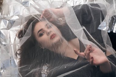 Tombul bir kızın güzel makyajı tül kumaşın altında altın bir folyonun üzerinde yatıyor..