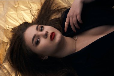 Tombul bir kızın güzel makyajı altın bir folyonun üzerinde yatıyor..