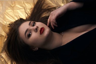 Tombul bir kızın güzel makyajı altın bir folyonun üzerinde yatıyor..