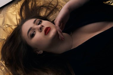 Tombul bir kızın güzel makyajı altın bir folyonun üzerinde yatıyor..