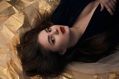 Tombul bir kızın güzel makyajı altın bir folyonun üzerinde yatıyor..