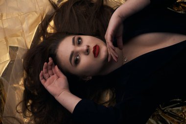 Tombul bir kızın güzel makyajı altın bir folyonun üzerinde yatıyor..