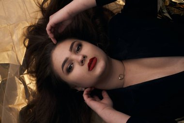 Tombul bir kızın güzel makyajı altın bir folyonun üzerinde yatıyor..