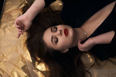 Tombul bir kızın güzel makyajı altın bir folyonun üzerinde yatıyor..