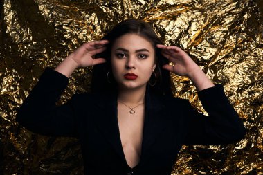 Altın bir arka planda siyah ceketli şık tombul bir kız..