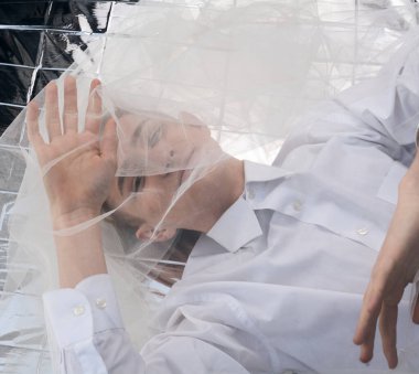 Yakışıklı bir manken gümüş folyoda tül kumaşın altında yatıyor..