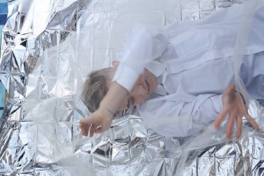 Yakışıklı bir manken gümüş folyoda tül kumaşın altında yatıyor..