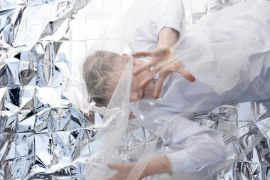 Yakışıklı bir manken gümüş folyoda tül kumaşın altında yatıyor..