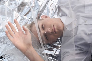 Yakışıklı bir manken gümüş folyoda tül kumaşın altında yatıyor..