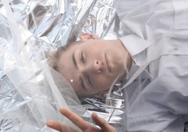 Yakışıklı bir manken gümüş folyoda tül kumaşın altında yatıyor..