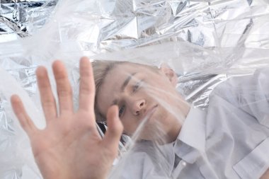 Yakışıklı bir manken gümüş folyoda tül kumaşın altında yatıyor..