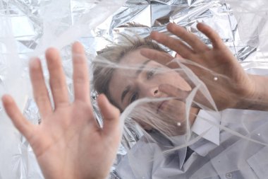 Yakışıklı bir manken gümüş folyoda tül kumaşın altında yatıyor..