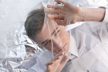 Yakışıklı bir manken gümüş folyoda tül kumaşın altında yatıyor..