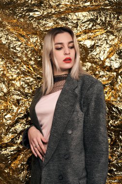 Altın bir arka planda ceketle poz veren şık bir kız..