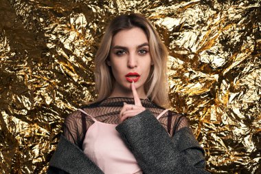 Altın bir arka planda ceketle poz veren şık bir kız..