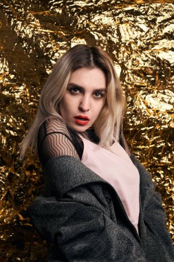 Altın bir arka planda ceketle poz veren şık bir kız..