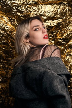 Altın bir arka planda ceketle poz veren şık bir kız..