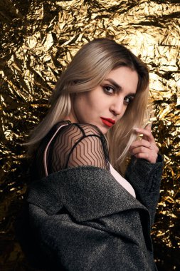 Altın bir arka planda ceketle poz veren şık bir kız..