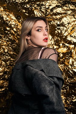 Altın bir arka planda ceketle poz veren şık bir kız..