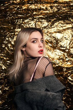 Altın bir arka planda ceketle poz veren şık bir kız..