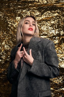 Altın bir arka planda ceketle poz veren şık bir kız..