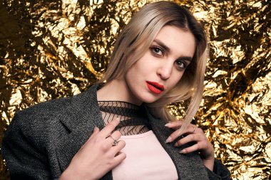 Altın bir arka planda ceketle poz veren şık bir kız..