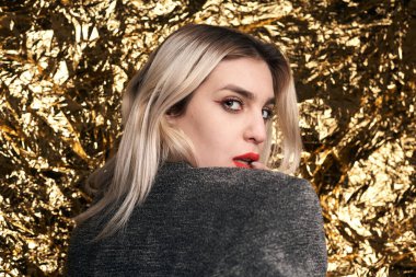 Altın bir arka planda ceketle poz veren şık bir kız..