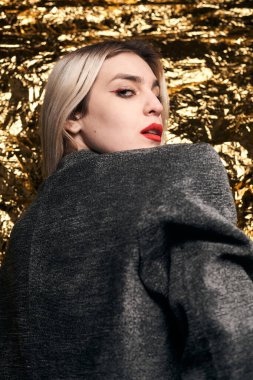 Altın bir arka planda ceketle poz veren şık bir kız..