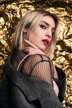 Altın bir arka planda ceketle poz veren şık bir kız..